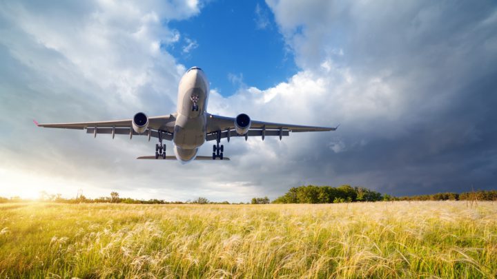 Airplane. Landscape with big white passenger airplane is flying in the blue sky over yellow grass field at colorful sunset in summer. Passenger airplane is landing. Business trip. Commercial aircraft