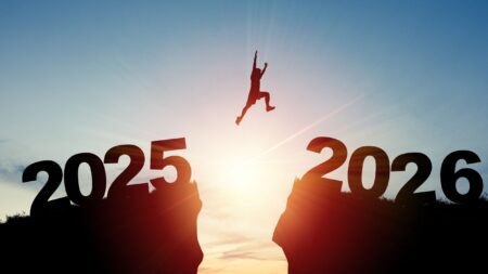 Silhouette Man jumping from 2025 cliff to 2026 cliff with cloud sky and sunlight. stock photo
